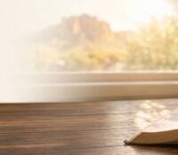 Open Bible and coffee mug on a wooden table at sunrise, with Superstition Mountain visible through the window, Day of Prayer at Superstition Foothills Baptist Church Gold Canyon AZ